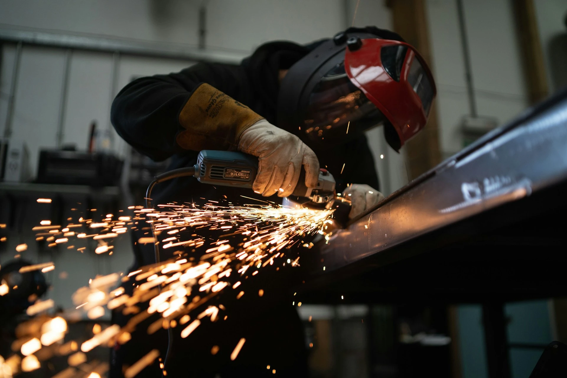 Metal fabricator grinding structural steel as sparks fly in a fabrication shop